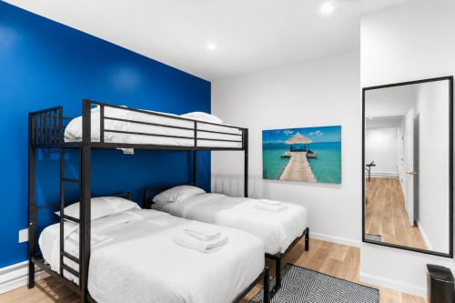 Modern bedroom with blue accent wall, black bunk beds, white linens, tropical beach art, and wooden flooring at Malkita Homes