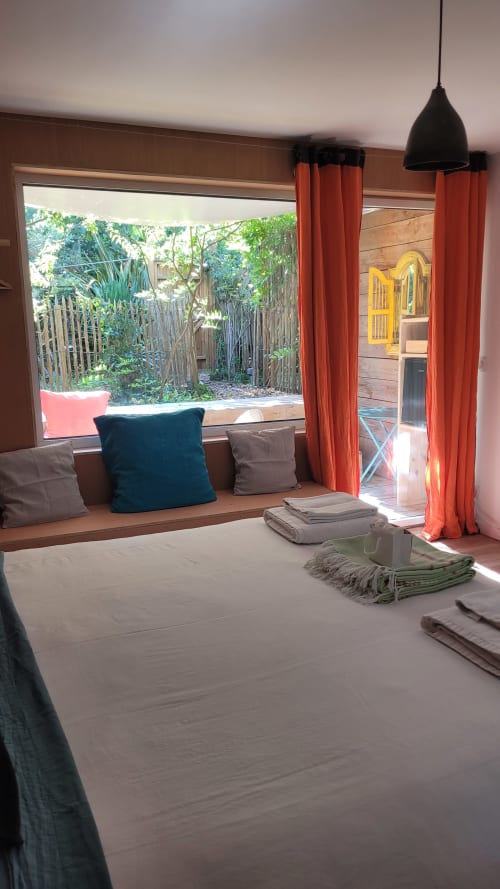 Chambre avec banquette à la fenêtre donnant sur le jardin au Lodge du Cap Ferret, suite Wise Monkey aux rideaux et coussins rouges