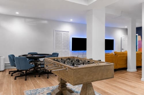 Modern game room at Malkita Terra villa in Woodbury with foosball table, pool table, gaming chairs, TVs, and mustard seating.