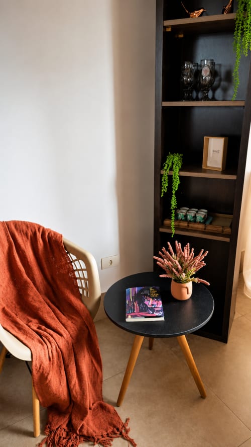 Área de estar moderna no CSS em Maringá com prateleiras pretas, planta em vaso, mesa redonda e manta laranja.