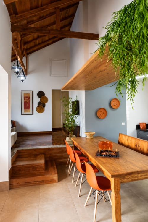 Sala de jantar moderna com mesa de madeira, cadeiras laranja, vigas aparentes e plantas verdes no apartamento CSS em Maringá