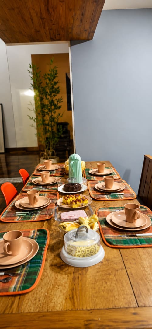 Mesa de jantar preparada para café da manhã no apartamento CSS em Maringá, com individuais xadrez, xícaras de café e salgados frescos