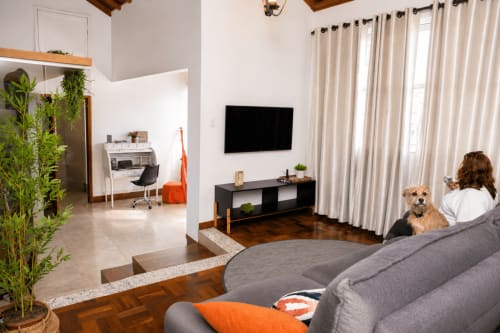 Sala moderna em apartamento em Maringá com sofá cinza, TV de tela plana, plantas em vasos e grandes janelas com cortinas