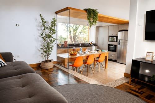 Apartamento moderno de planta aberta em Maringá com ilha de cozinha em madeira, cadeiras laranja, sofá cinza e vista para a cidade através de vidro