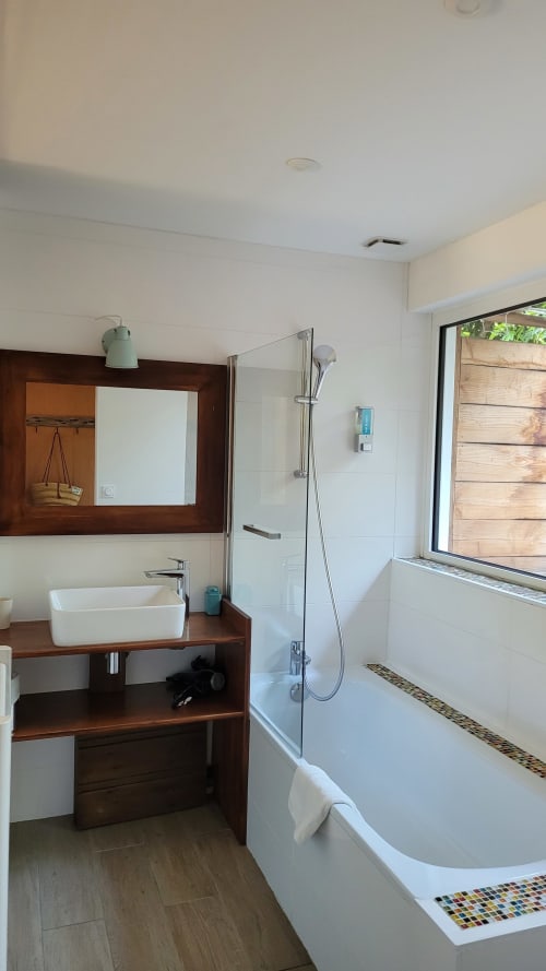 Bagno moderno con vanity in legno, lavabo bianco, vasca da bagno, doccia in vetro e vista sul giardino presso Le Lodge du Cap Ferret