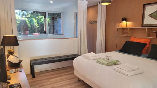 Camera moderna al Lodge du Cap Ferret con letto bianco, dettagli arancioni, finestre con vista sul giardino e pavimenti in legno