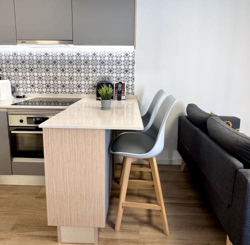 Cuisine moderne avec coin salon dans l'appartement RIA CENTRUM Premium Silver, îlot central, tabourets et canapé gris