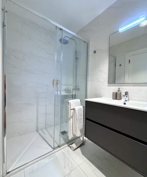 Salle de bain moderne avec carrelage en marbre, douche vitrée, vasque noire et miroir à RIA CENTRUM Smart Residence