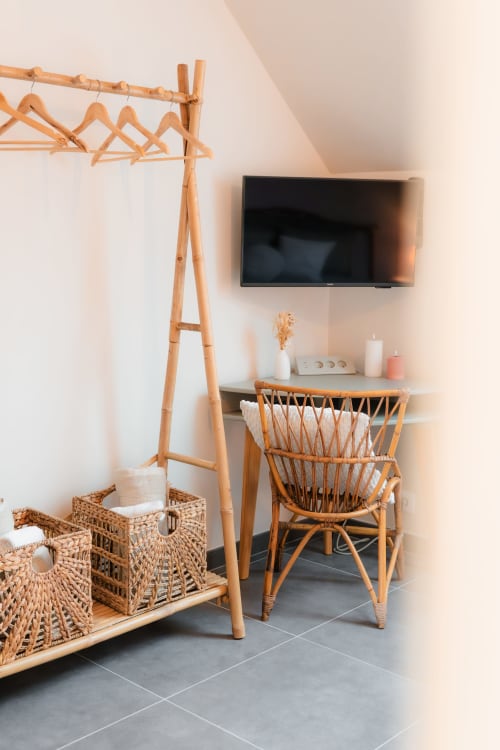 Coin cosy de la chambre au gîte Le Hameau de Céline avec portant en bois, paniers en osier, fauteuil en rotin et TV murale