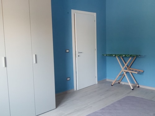 Camera da letto moderna con pareti blu, porta bianca, asse da stiro in legno e pavimento in legno chiaro presso My Home Apulia, Veglie