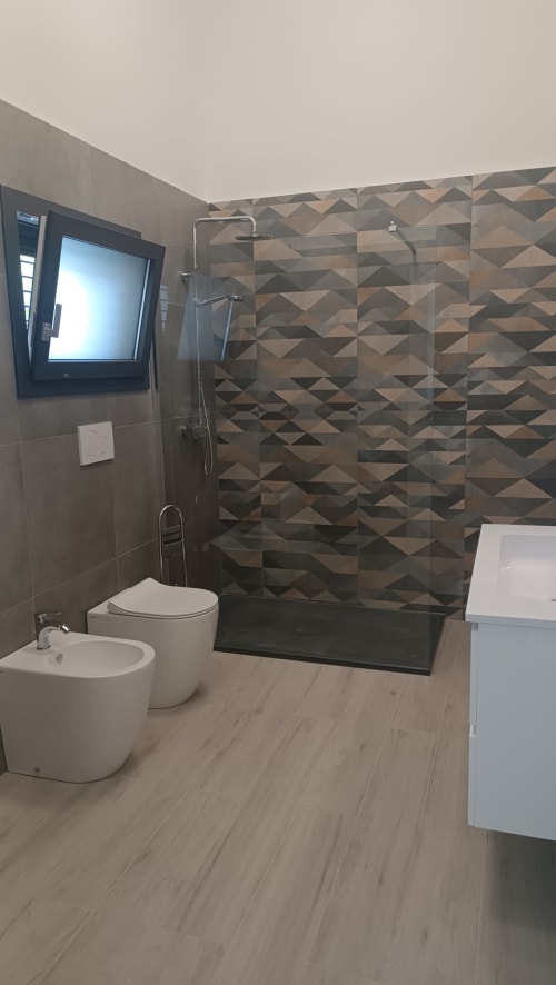 Bagno moderno a My Home Apulia Amelia Blue con doccia in piastrelle geometriche, wc, bidet e pavimento effetto legno