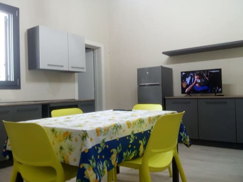 Luminosa zona living dell'appartamento Amelia Blue presso My Home Apulia con sedie gialle, tovaglia floreale, cucina e TV