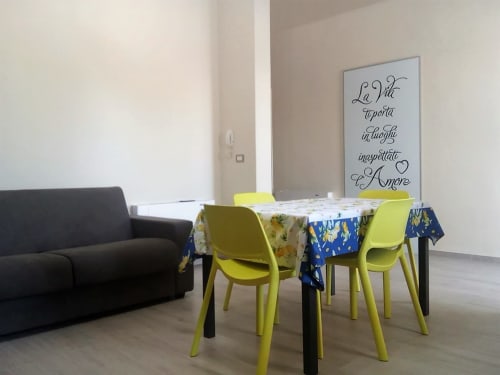Zona pranzo con sedie gialle e tovaglie a fantasia presso l'appartamento My Home Apulia a Veglie, con arte murale motivazionale