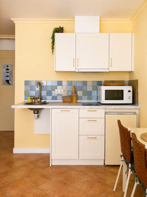 Cocina compacta moderna en apartamento de Baiona con muebles blancos, azulejos azules, microondas y paredes amarillas