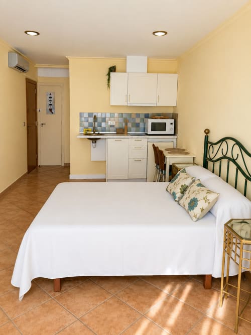 Apartamento estudio luminoso en Baiona con cama, cocineta, muebles blancos, azulejos azules y mobiliario de madera