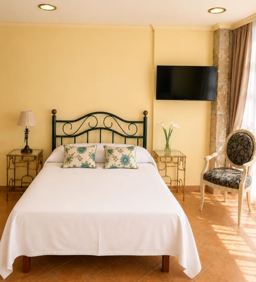 Dormitorio luminoso en apartamento Holibai de Baiona con cama de hierro forjado, paredes amarillas, TV y silla decorativa