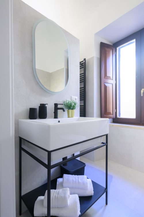 Bagno moderno presso Almatros Rubino Design Suites a Sulmona con specchio ovale, rubinetteria nera e asciugamani bianchi