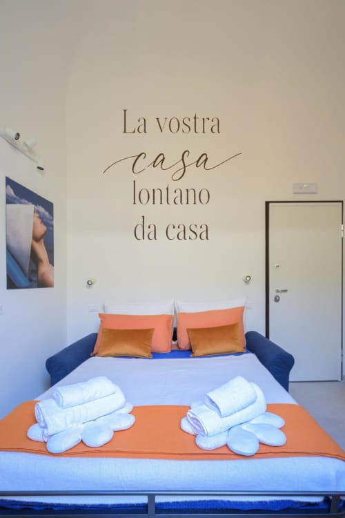 Camera moderna presso Almatros Sulmona con letto blu, accenti arancioni, asciugamani di benvenuto e arredamento murale italiano