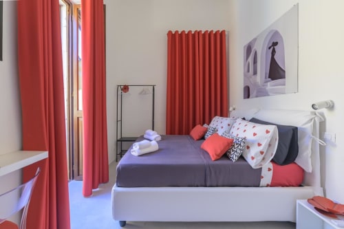 Suite Rubino dell'hotel Almatros a Sulmona con tende rosse, letto viola e arredamento moderno