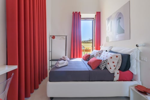 Camera Rubino Design Suite dell'hotel Almatros a Sulmona con tende rosse, letto scuro e vista sulla valle