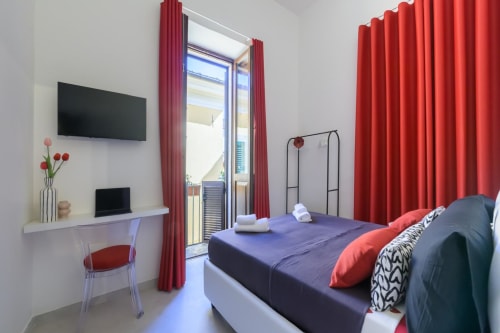 Camera moderna presso Almatros Rubino Design Suites a Sulmona con tende rosse, letto viola, scrivania con TV e accesso al balcone