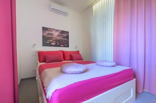 Camera da letto moderna e luminosa presso Almatros Tormalina Design Suites a Sulmona con biancheria rosa, cuscini viola e finestre a tutta altezza