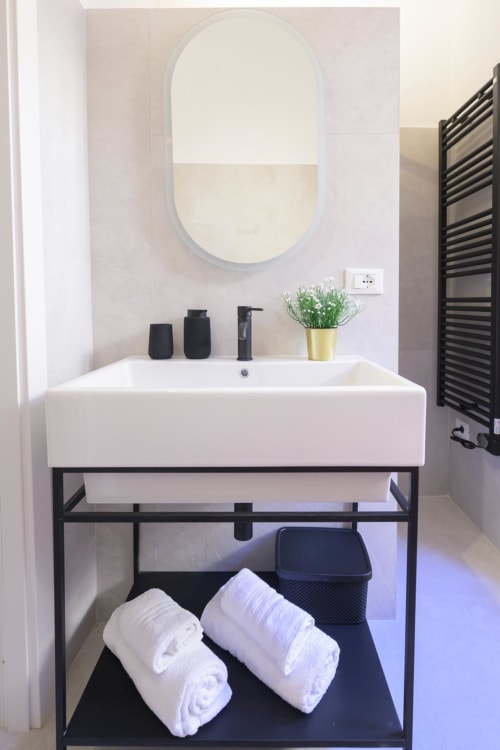 Bagno moderno dell'hotel Almatros a Sulmona con specchio ovale, lavabo bianco, rubinetteria nera e asciugamani arrotolati