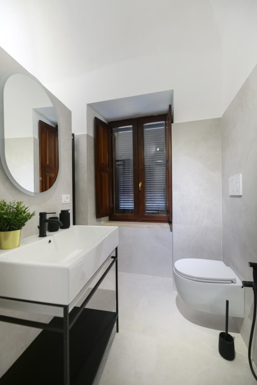 Bagno moderno della Rubino Design Suite all'hotel Almatros di Sulmona con lavabo bianco, wc e specchio ovale con dettagli scuri
