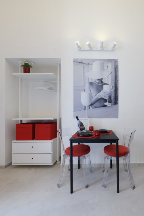 Moderna zona pranzo della Rubino Design Suites, hotel Almatros, Sulmona con tavolo nero, sedie rosse e mobile contenitore bianco.