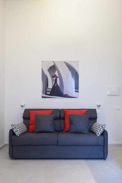 Elegante divano scuro con cuscini rossi nella suite Rubino Design di Almatros, Sulmona, con arte astratta alle pareti