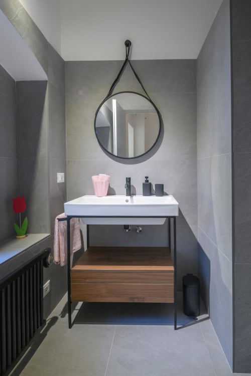 Bagno moderno nelle Tormalina Design Suites dell'hotel Almatros a Sulmona, con specchio circolare, lavabo bianco e mobile in legno