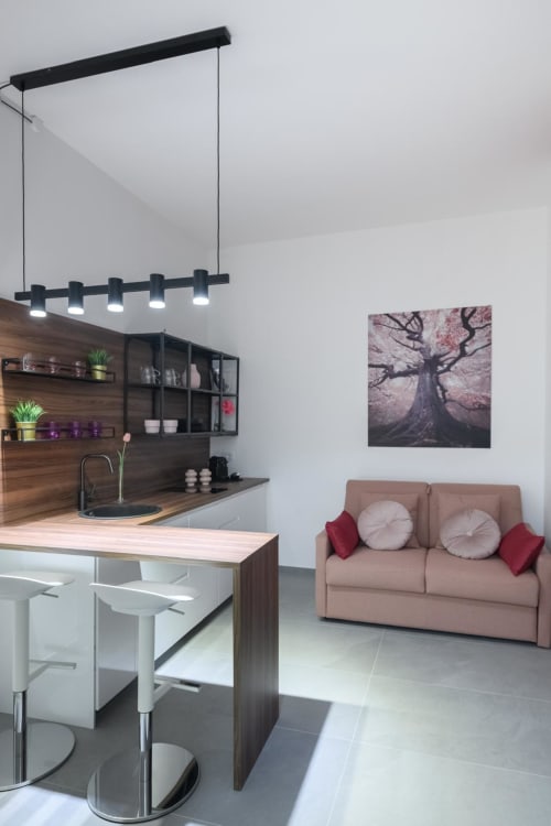 Cucina moderna con mobili in noce, lampade a sospensione nere, divano rosa con cuscini e quadro con albero a Tormalina