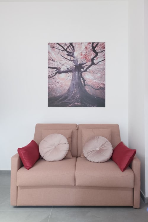 Divano beige con cuscini rotondi e sedute borgogna sotto una fotografia di albero rosa presso l'Almatros Hotel di Sulmona