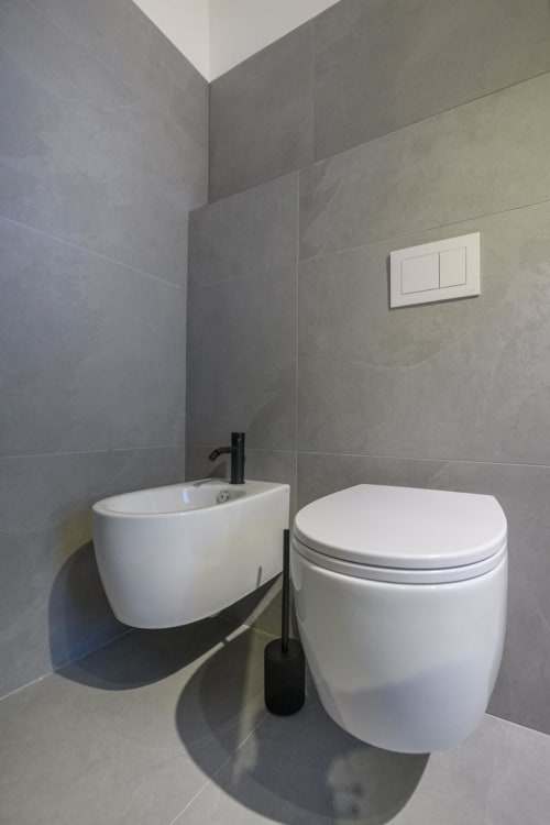 Bagno moderno alle Almatros Tormalina Design Suites a Sulmona con WC bianco, bidet, rubinetteria nera e piastrelle grigie