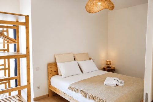Quarto luminoso na Terra Clara Studios com cama de madeira, roupas de cama brancas, manta bege, luminária de palha pendente e vista para o mar