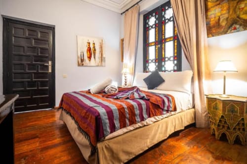Chambre de luxe à La Villa El Gada à Marrakech avec literie rayée colorée, vitrail, parquet et