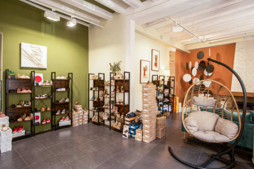 Tienda de boutique hotelero moderno con pared verde, estanterías decorativas, platos colgantes y silla mecedora tejida.