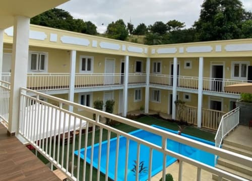 Pátio do Hotel PZero em Albufeira com edifícios amarelos, corrimãos brancos e passagens cobertas azuis cercadas por árvores