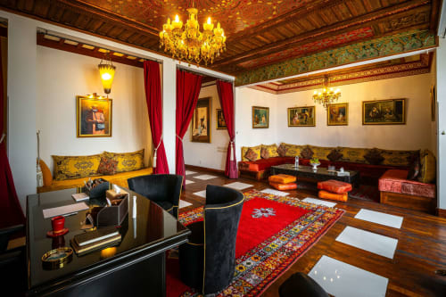 Salon luxueux de la Villa El Gada à Marrakech avec plafond orné, lustre doré, sièges traditionnels et motifs rouges