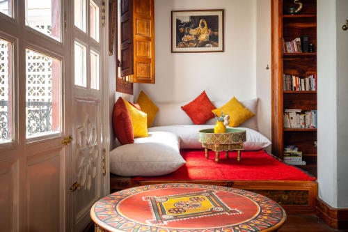 Coin lecture douillet à la Villa El Gada à Marrakech avec coussins colorés, tapis rouge et table basse décorée