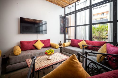 Salon marocain à Villa El Gada à Marrakech avec canapés rouges, coussins dorés et table en zellige géométrique