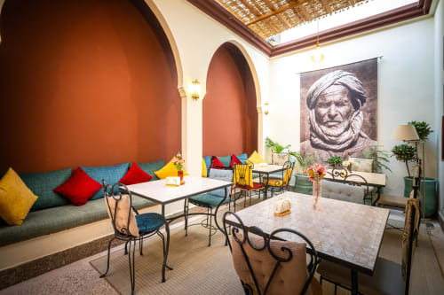 Cour de riad marocain à Villa El Gada avec alcôves cintrées, coussins colorés, chaises en fer forgé et portrait