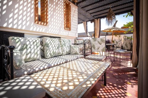 Terrasse ensoleillée de la Villa El Gada à Marrakech avec coussins à motifs, treillage ombragé et vue sur le jardin désertique