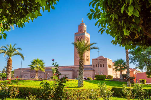 Villa El Gada à Marrakech avec le minaret emblématique de la Mosquée Koutoubia, jardins luxuriants et palmiers sous un ciel bleu dégagé