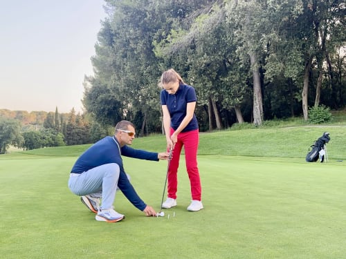 Instructeur de golf enseignant à une golfeuse sur le parcours de STAYnGOLF Cagnes sur Mer avec arbres et greens en arrière-plan