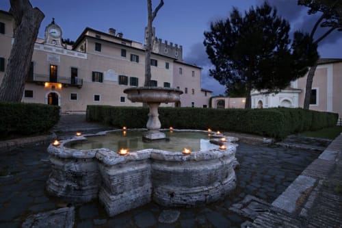 Cortile storico della Maison Tizi a Fiumicino Roma, con fontana illuminata e architettura in pietra al crepuscolo