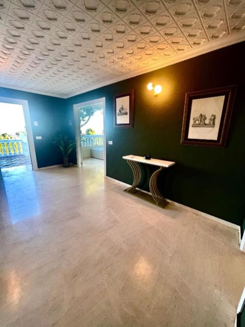 Sala de estar de villa moderna con paredes turquesas, vistas al océano a través de puertas de balcón, techo decorativo, consola y marco