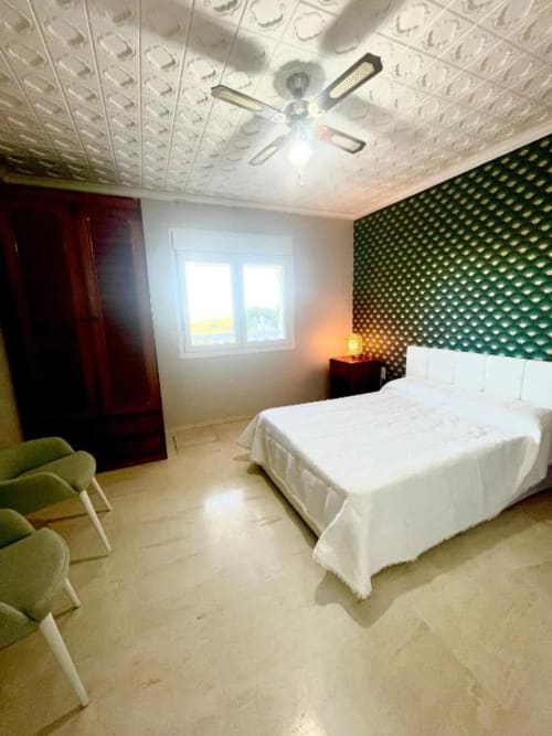 Dormitorio de villa moderna con vistas al océano, cama blanca, pared de acento verde, ventilador de techo y luz natural desde ventana en Málaga