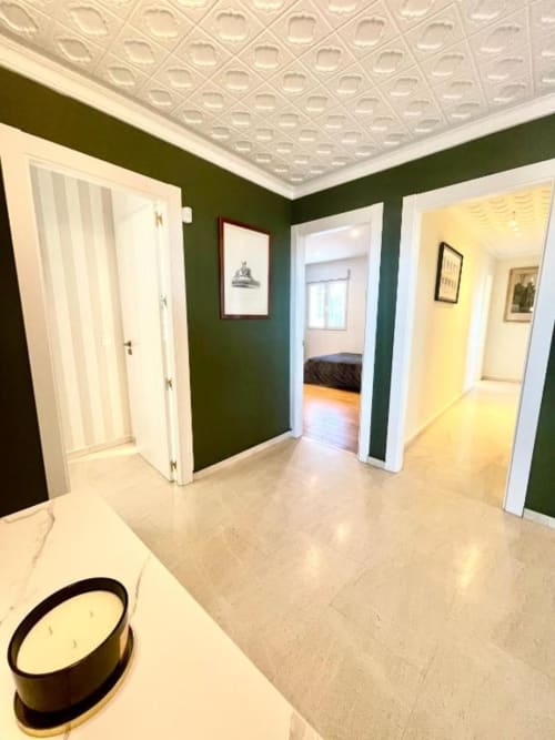 Pasillo espacioso en Villa Magos, Málaga con paredes verde bosque, puertas con molduras blancas, techo decorativo y suelo de azulejos.