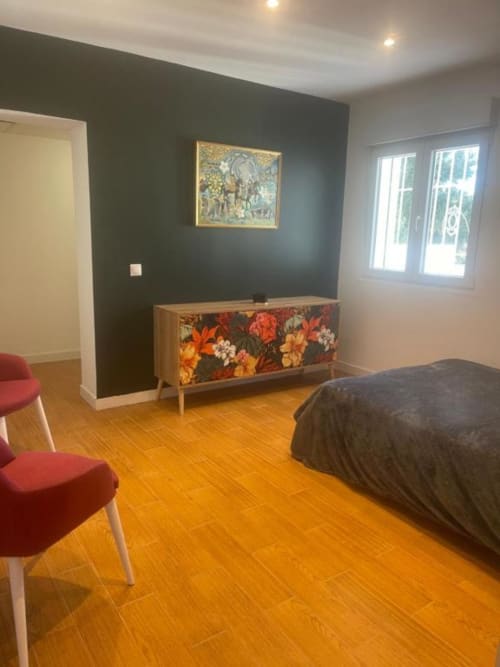 Dormitorio moderno en Villa Magos, Málaga, con suelo de baldosas naranjas, pared oscura de acento, cómoda floral y silla roja